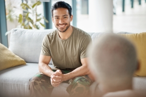 Smile, soldier and man with psychologist for therapy, consultation and military communication. Happy, army veteran and counselling with therapist for mental health, help or support on sofa in office.
