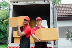 indian and caucasian partnership mover workers in red uniform uploading furniture and boxes to new house
