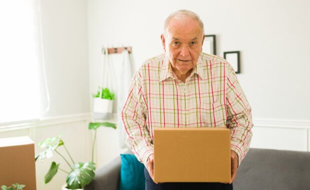 happy old man holding a box while moving into a new apartment or home