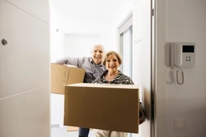 smiling senior couple carrying cardboard boxes while entering their new home